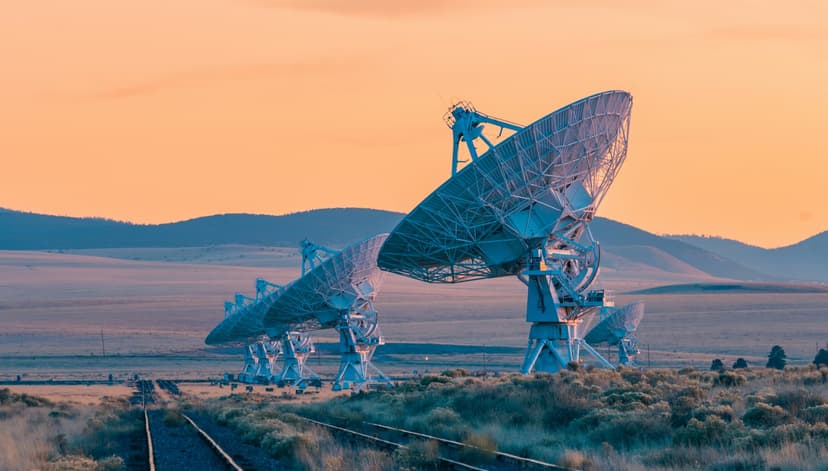 Satellite dishes silhouetted against a vibrant sunset in a desert landscape.